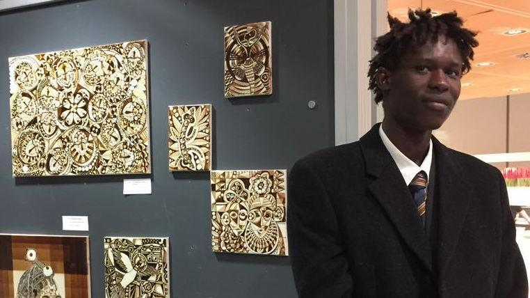Il giovane artista gambiano Abdoukhadre Ba e, sullo sfondo, alcune delle sue opere